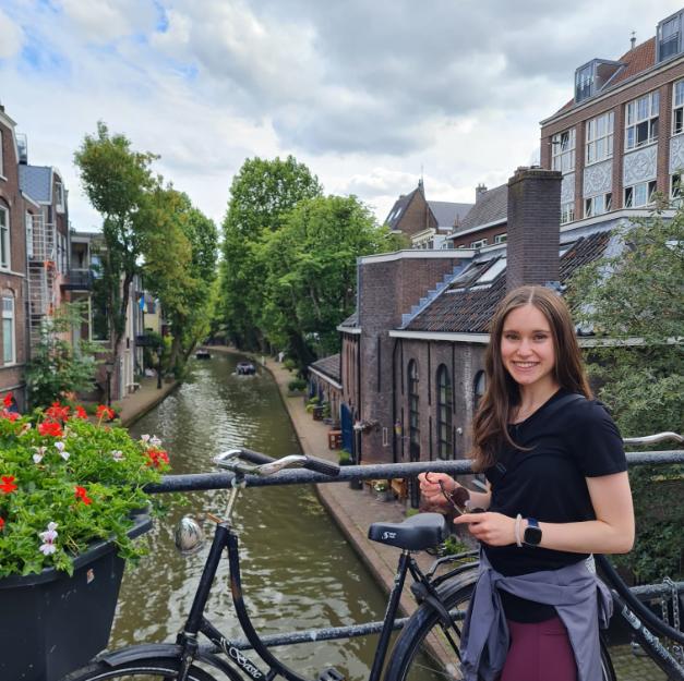 A student, Heidi Simpson, poses on a bridge next to a bike.